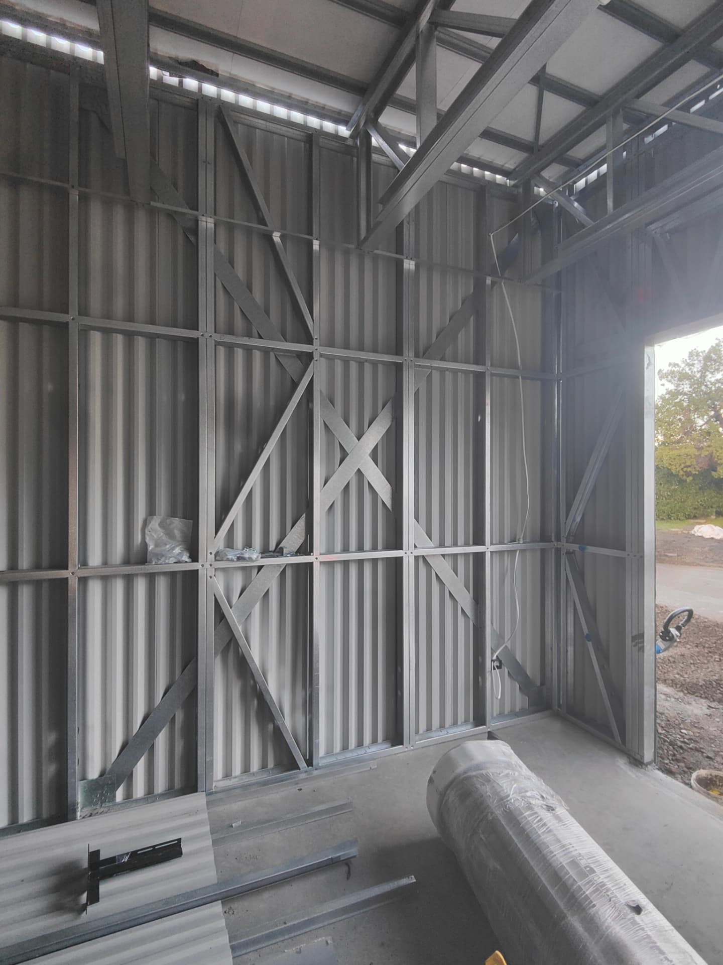 Steel stud wall framing with diagonal cross bracing inside a shed, with corrugated cladding and materials on the slab