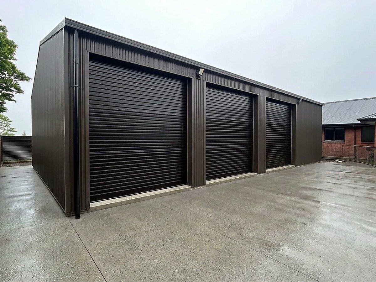 Three-bay bronze-clad workshop with three roller doors and a finished concrete apron, built by 03 Sheds and Garages in Canterbury