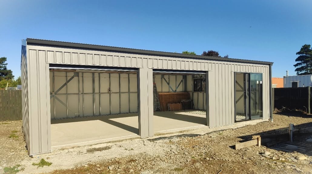 Inside a completed 03 garage with the roller doors open, showing steel framing, wall underlay and a concrete floor