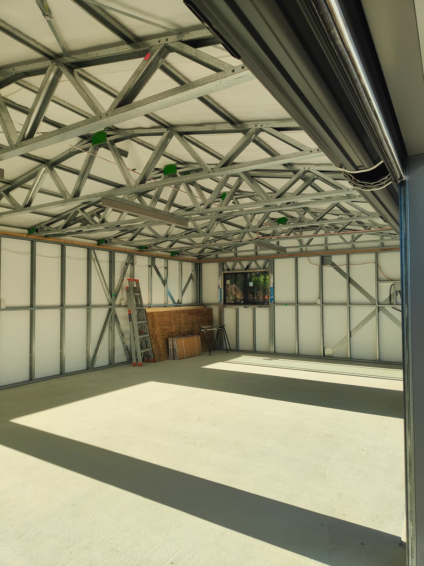 Steel roof trusses and lined steel stud walls inside a garage, seen through the open roller door