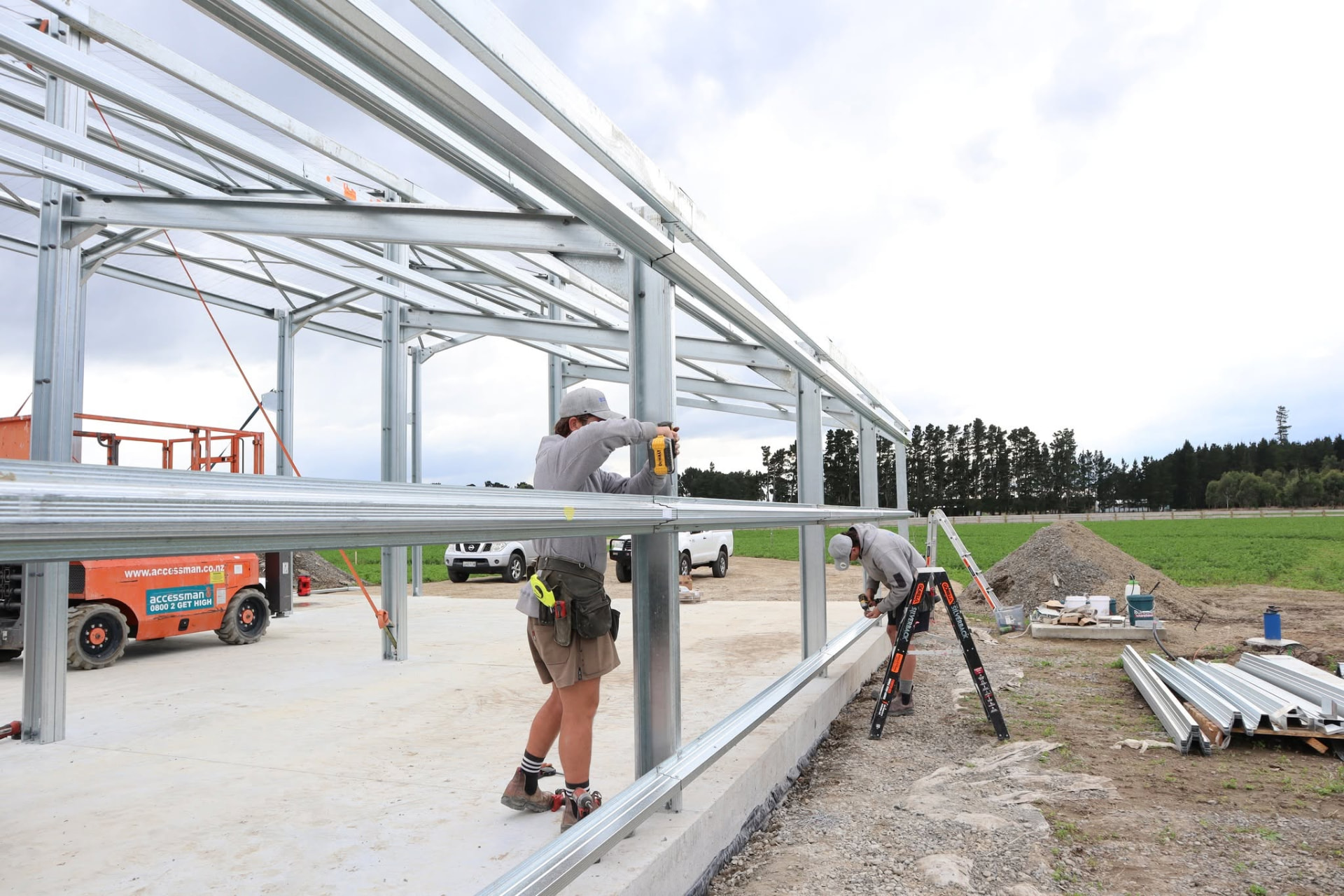 Builders fixing continuous top hat girts over the outside face of a steel shed's portal columns